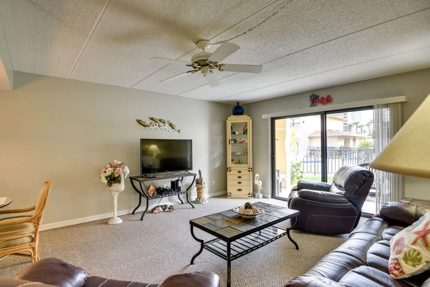 Living room with carpeted floors, leather seating, a coffee table, television, and sliding glass doors leading outside.