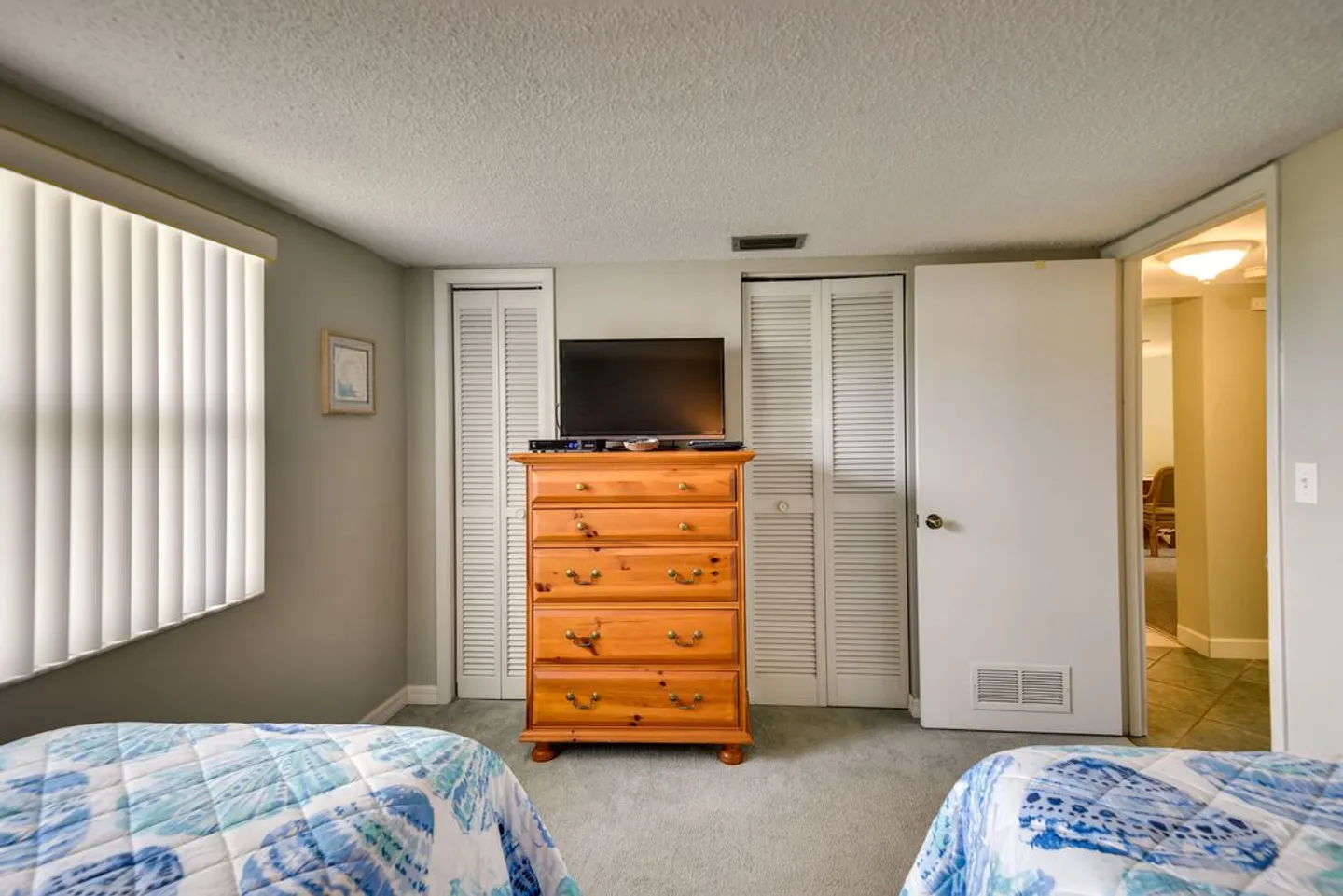 Bedroom featuring two beds with blue patterned quilts, a wooden dresser with a flat-screen TV, and closet doors with louvered panels.