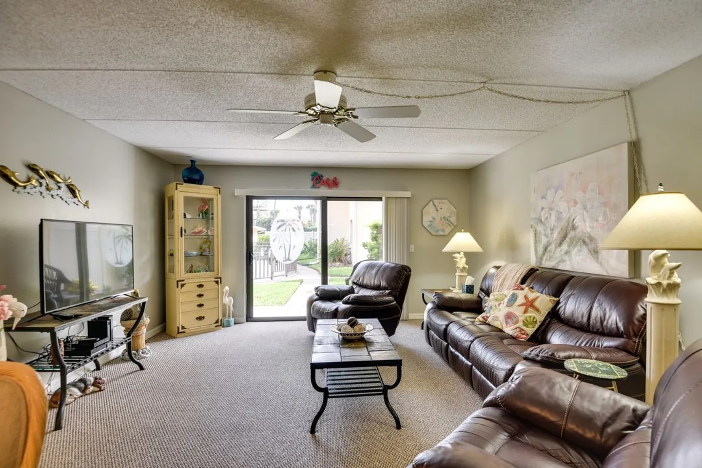 Living room with carpet, brown leather seating, a TV on a stand, and sliding glass doors leading outside.