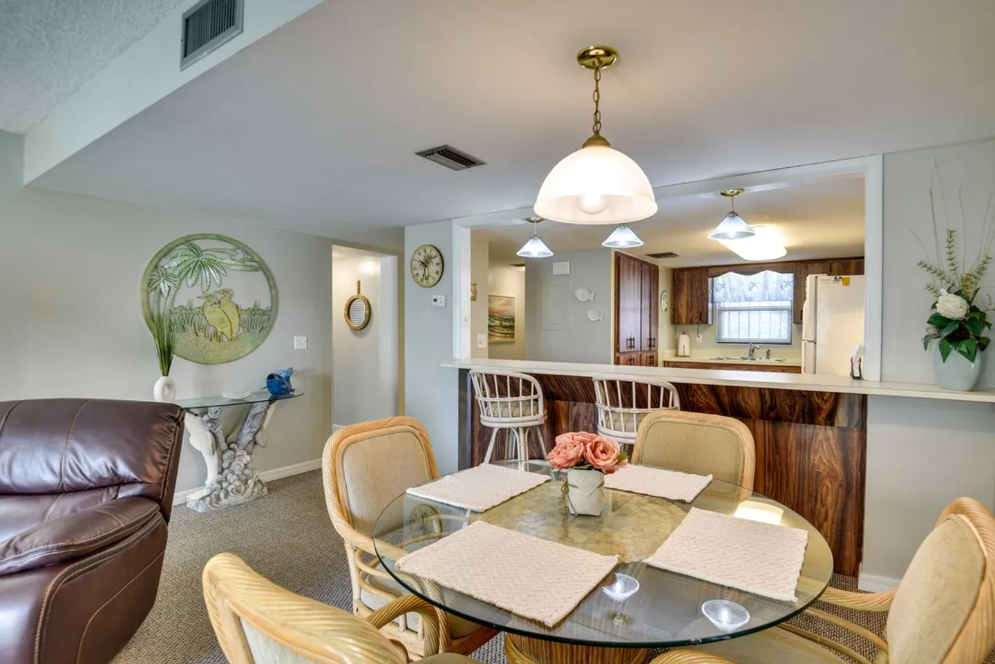 Dining area with a round glass-top table, wicker chairs, and a pass-through breakfast bar leading into the kitchen.