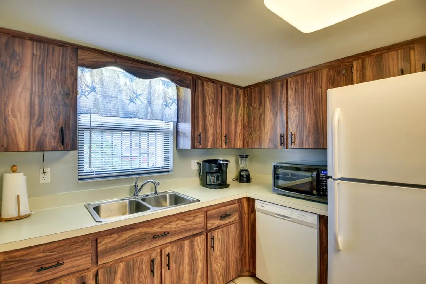Kitchen with wood-grain cabinets, double sink, white refrigerator, dishwasher, and microwave on the countertop.
