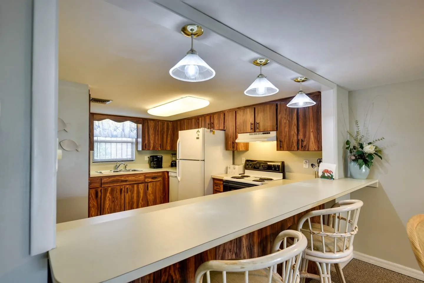 A kitchen viewed across a breakfast bar with light-colored stools and wood-toned cabinetry.