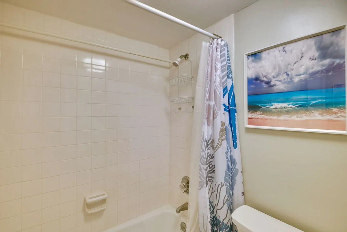 Bathroom showing a tiled tub and shower combination with a themed shower curtain and framed beach artwork on the wall.