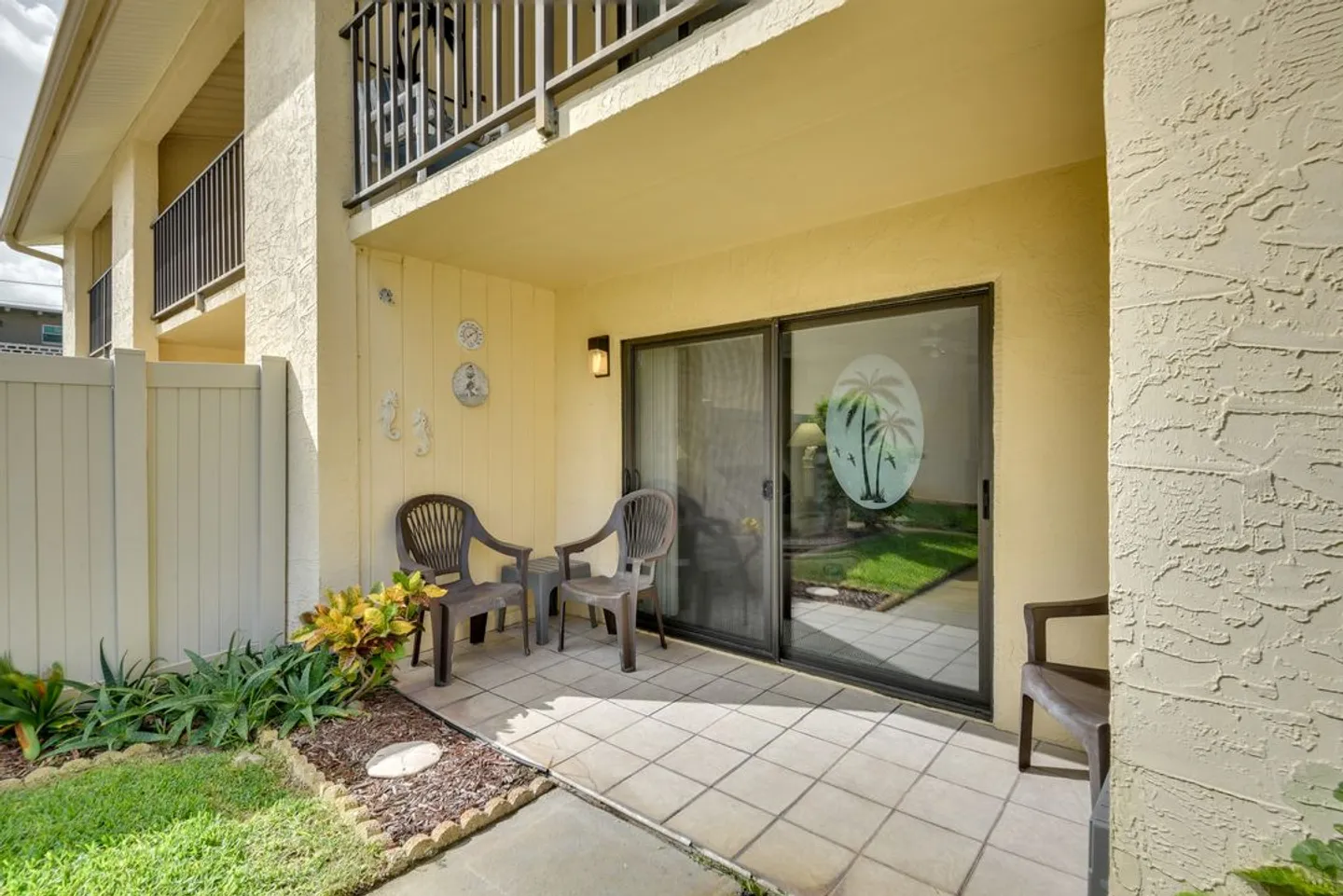 A tiled ground-floor outdoor patio with armchairs next to sliding glass doors.