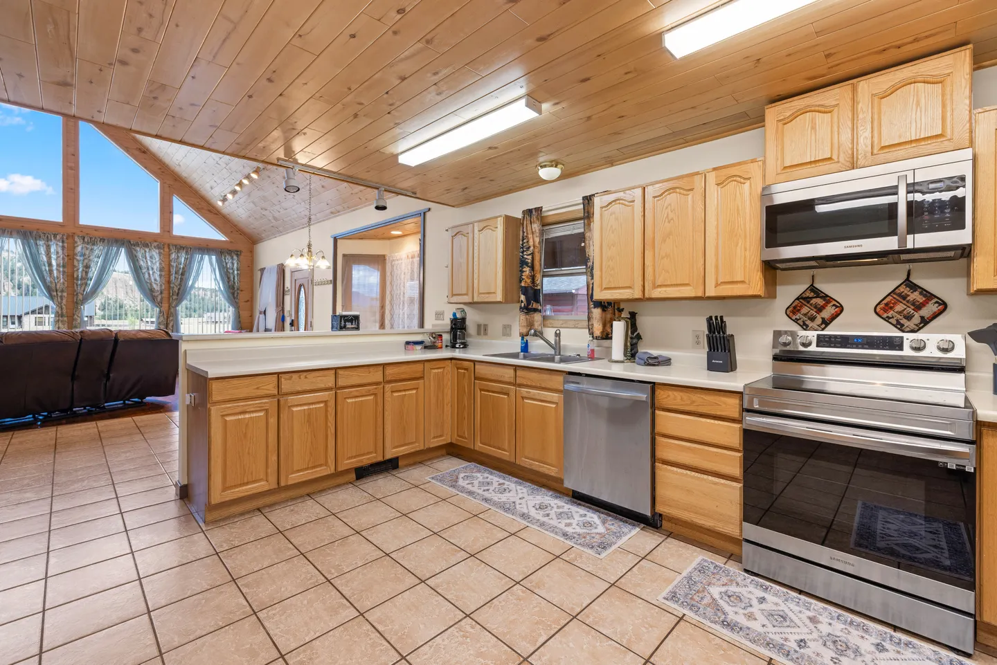 Kitchen with wooden cabinetry, tiled floors, wood-paneled ceiling, and a view into the adjoining living room.