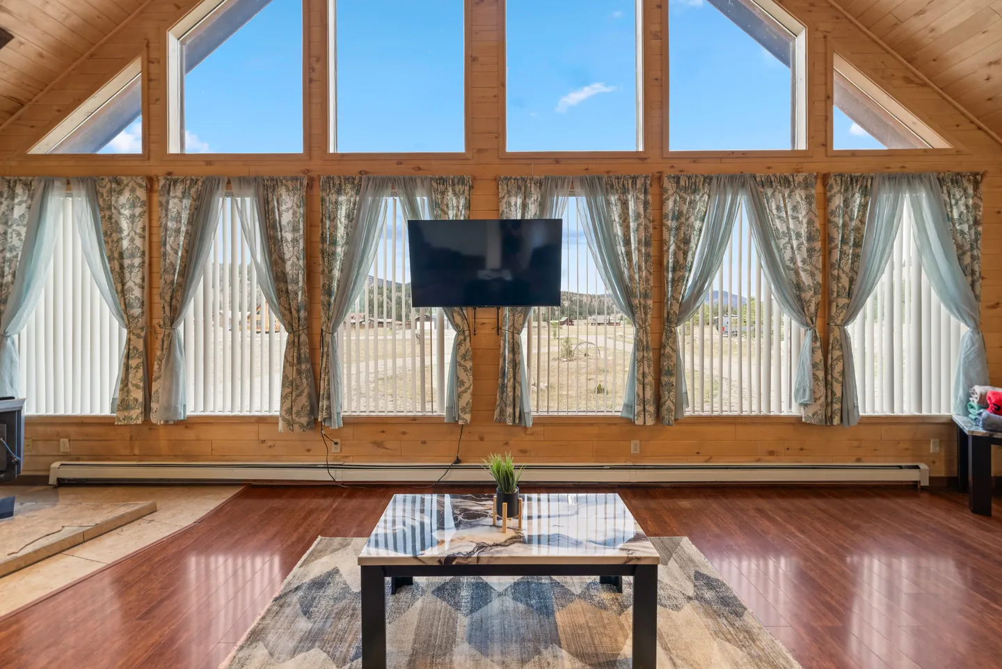 Living room featuring a large wall of windows with upper clerestory glass, wood paneling, a mounted TV, and a coffee table.