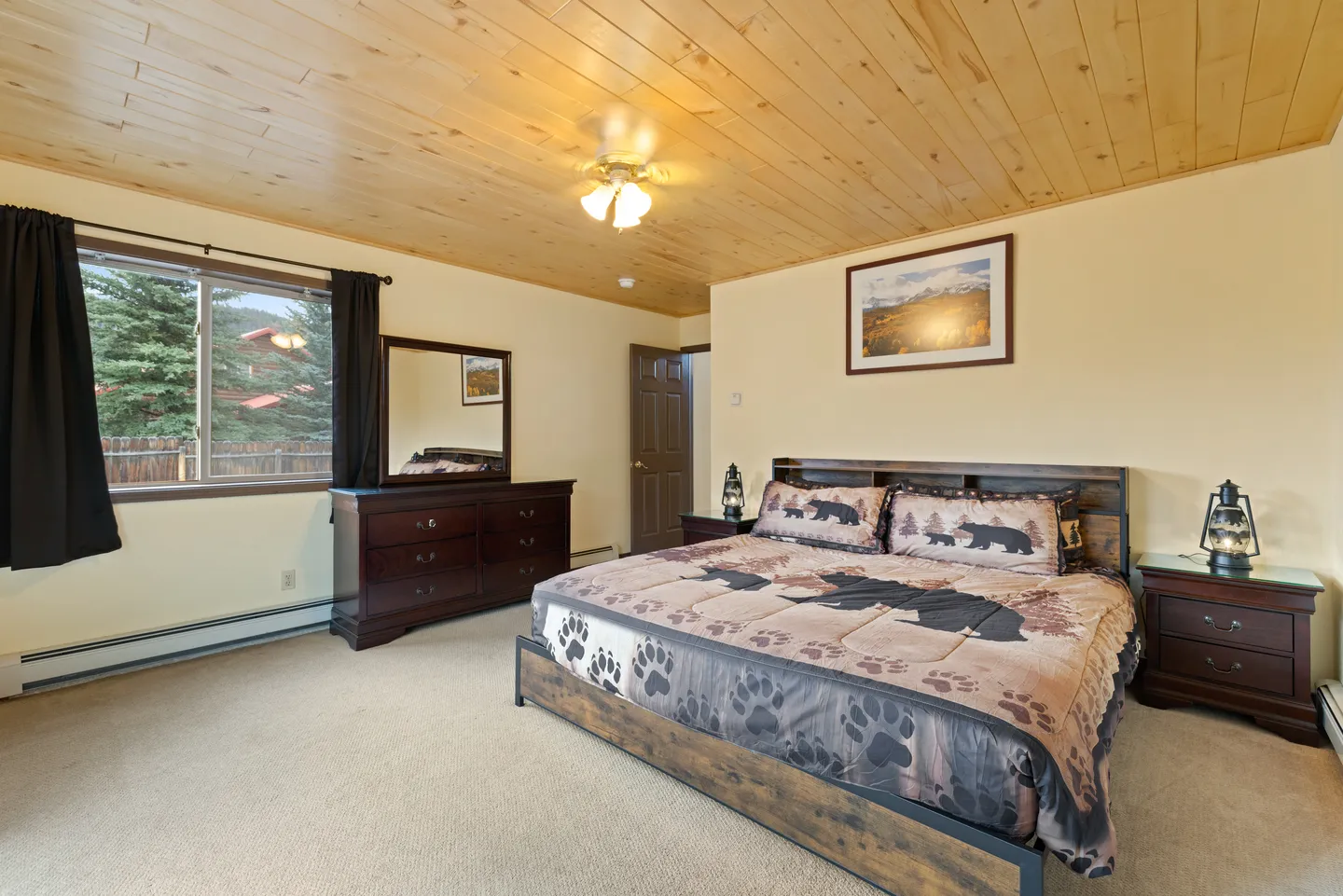 Bedroom with carpeted floor, light wood-paneled ceiling, a large bed with bear-themed bedding, a dresser, and matching nightstands.