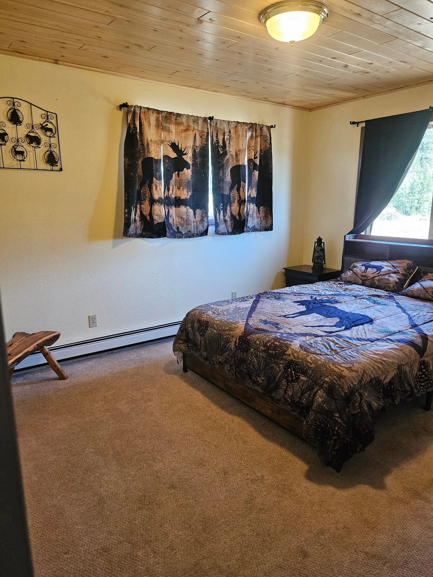 Bedroom featuring a wooden-plank ceiling, carpeted floor, bed with wildlife-themed bedding, and matching moose curtains.