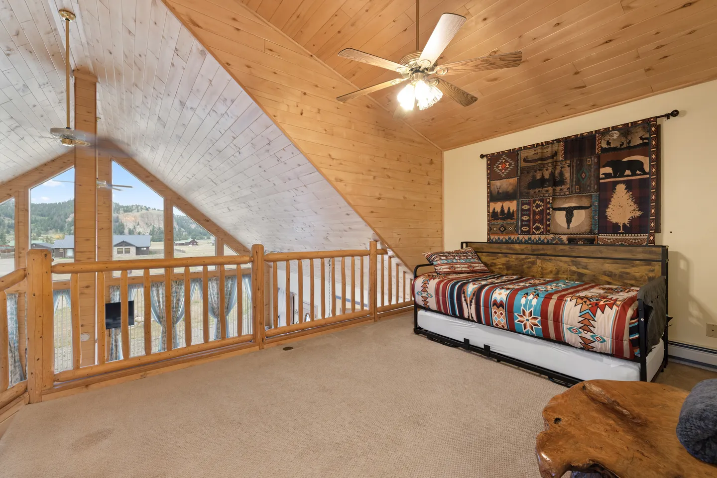 Open loft space featuring carpeted flooring, a log railing, angled wood ceilings, and a daybed with a trundle.