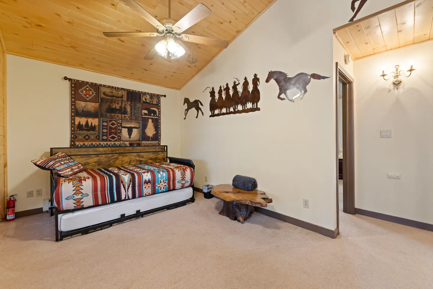 Bedroom featuring a daybed with a trundle, wood-paneled vaulted ceiling, ceiling fan, and Western-themed wall decor.