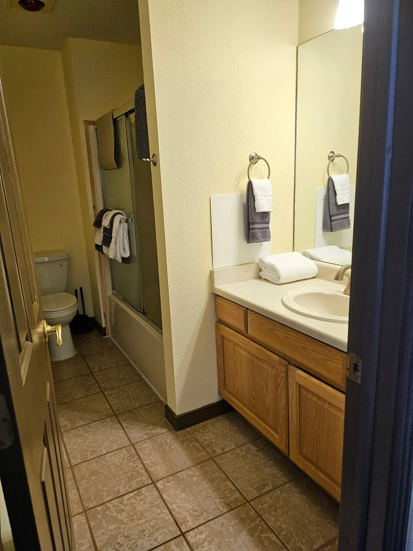 Bathroom with a wood vanity, tiled floor, a toilet in the back, and a glass-enclosed shower and tub combo.