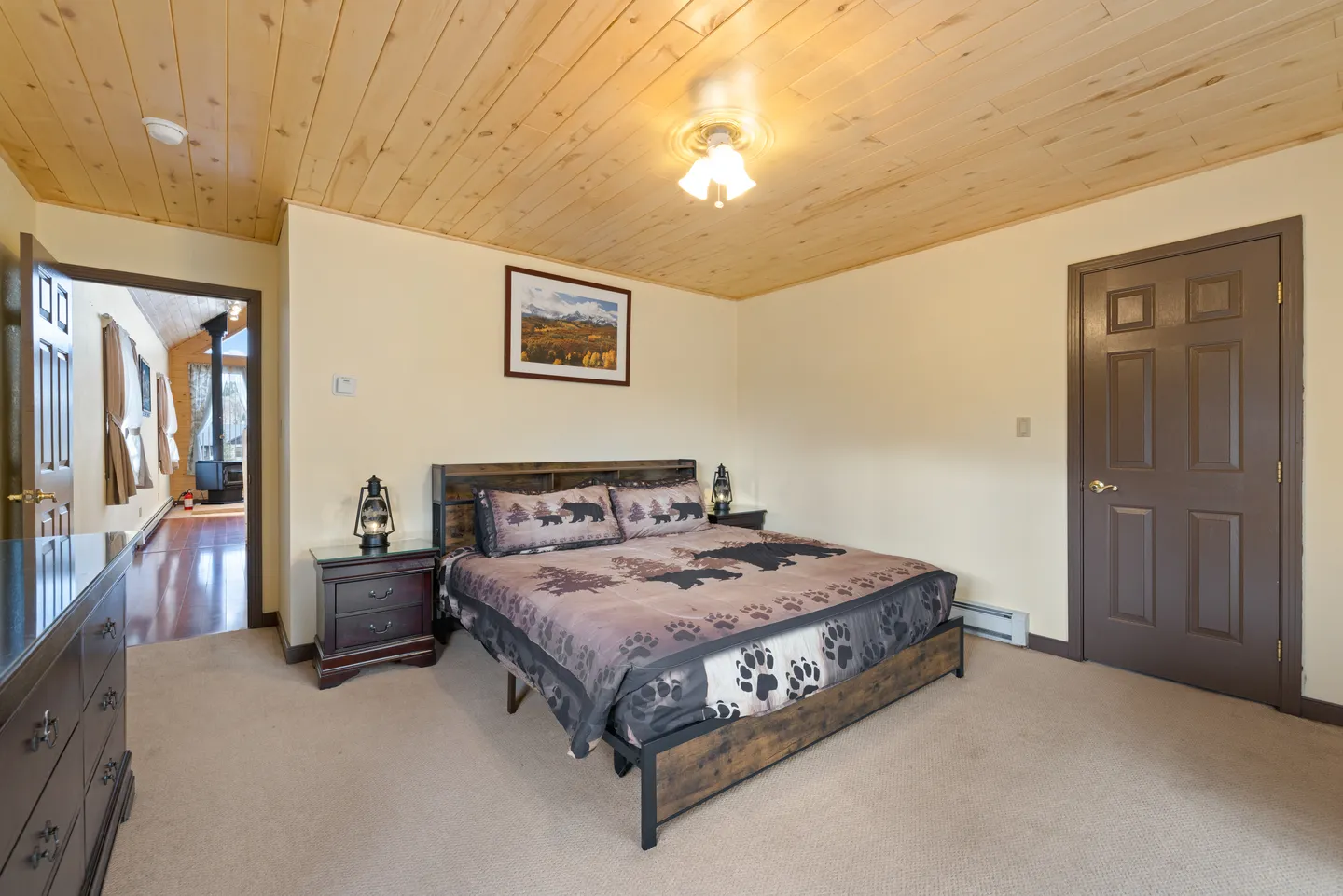 Bedroom featuring a wood-plank ceiling, carpeted floor, rustic bed frame with bear-print bedding, and a dark brown door.