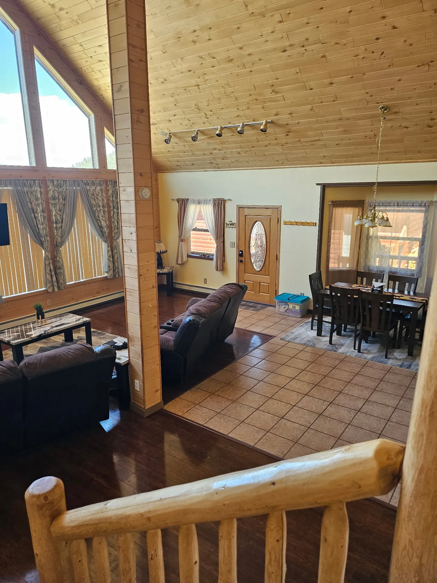 Elevated view from a staircase overlooking an open-concept living and dining area with vaulted wood ceilings.
