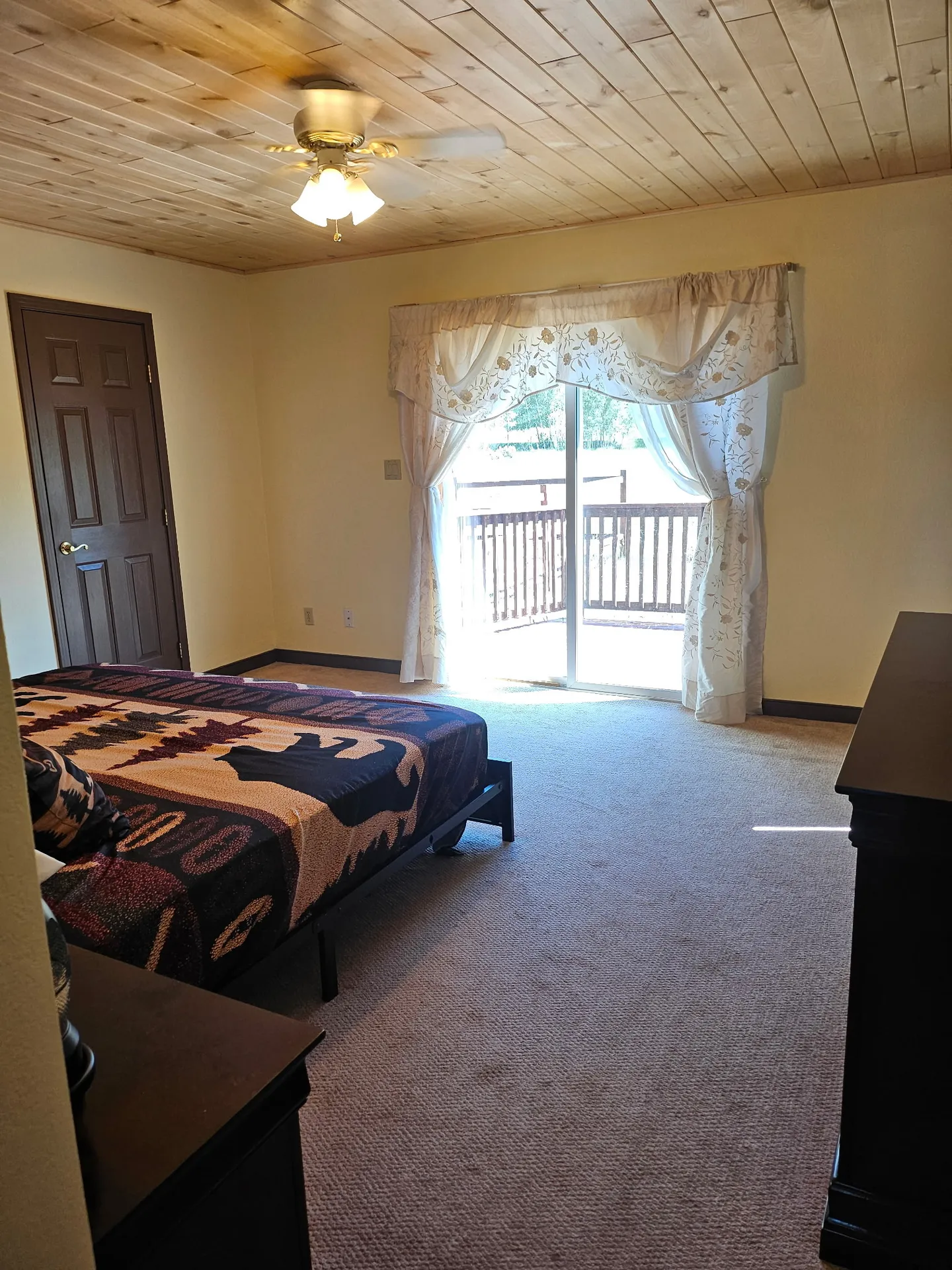 Bedroom featuring a wood-plank ceiling, carpeted flooring, a bed with a bear-patterned quilt, and sliding glass doors leading to a balcony.