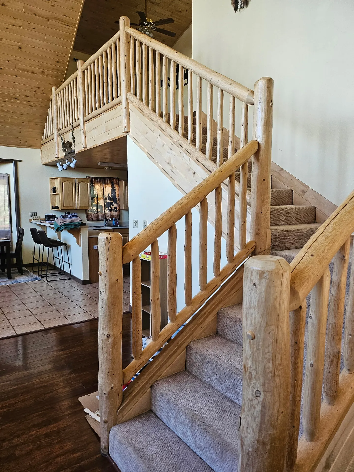 Carpeted staircase with log railings leading to a loft above a kitchen and dining area.