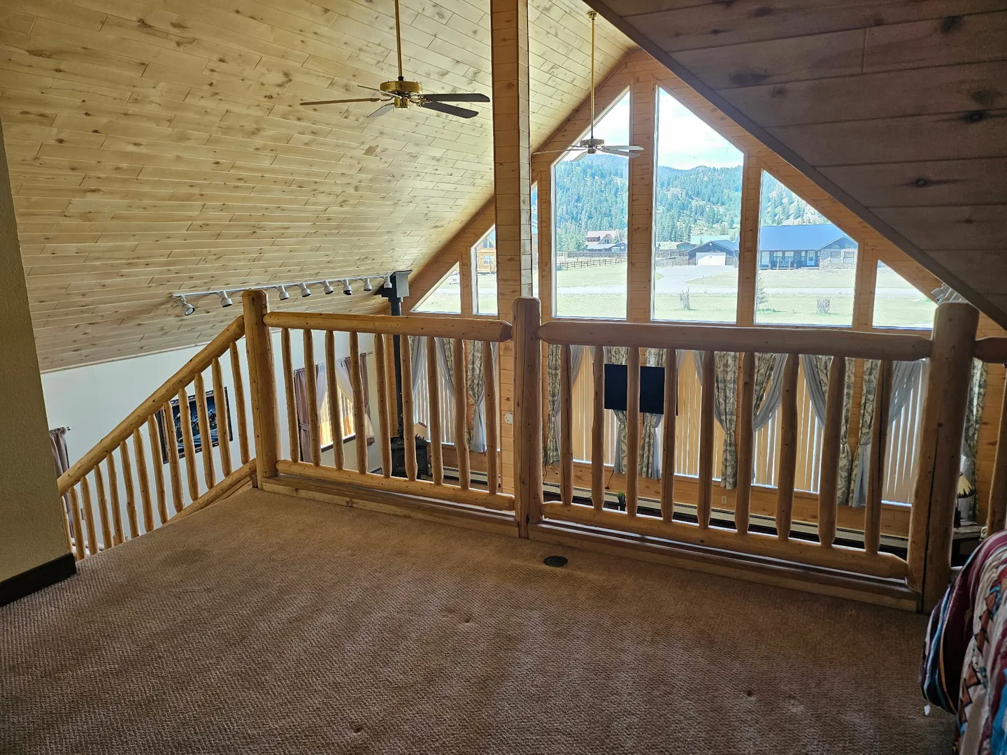 Upstairs carpeted loft with log railings overlooking large peaked windows with mountain views.
