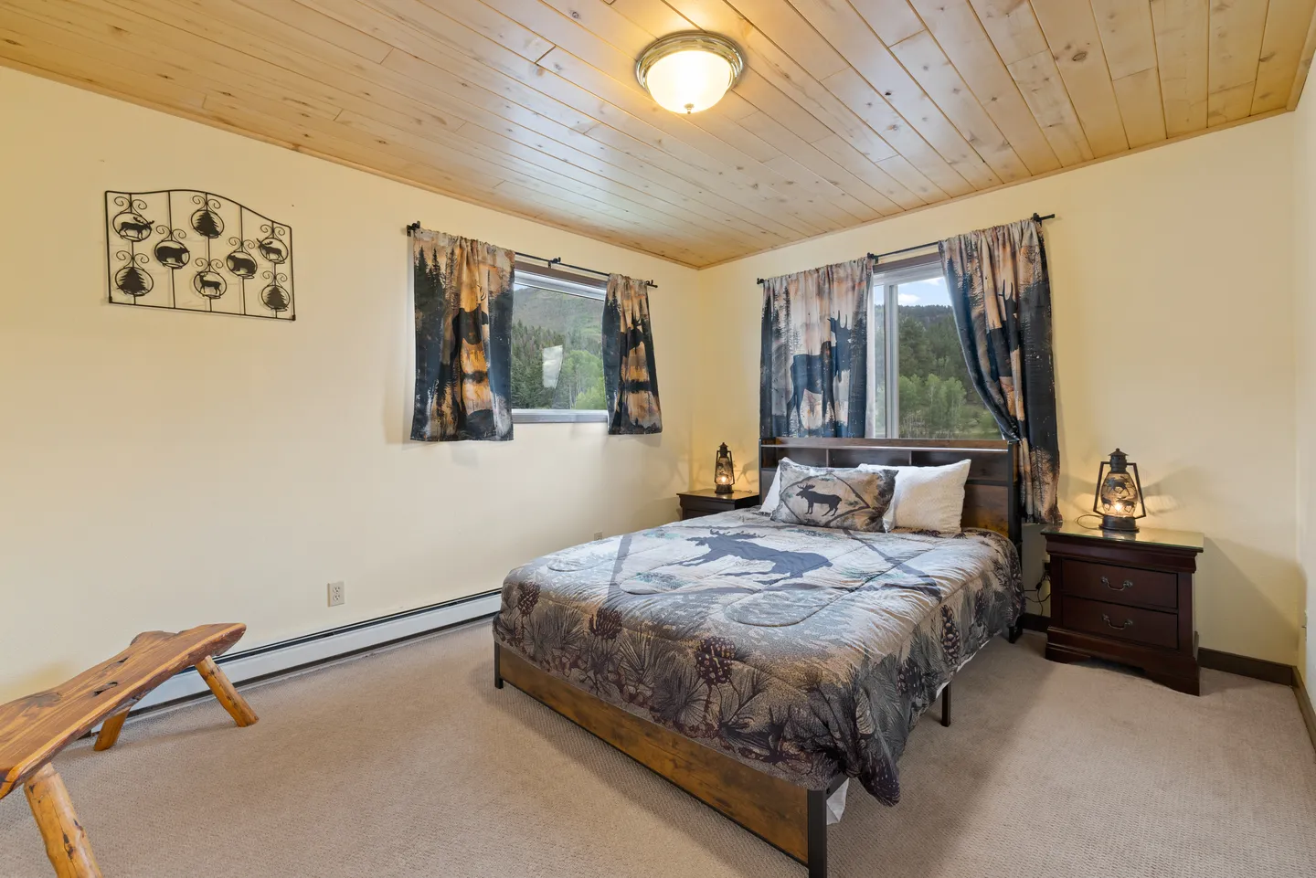 Bedroom with a wood-plank ceiling, carpeted floor, bed with nature-themed bedding, and matching window curtains.