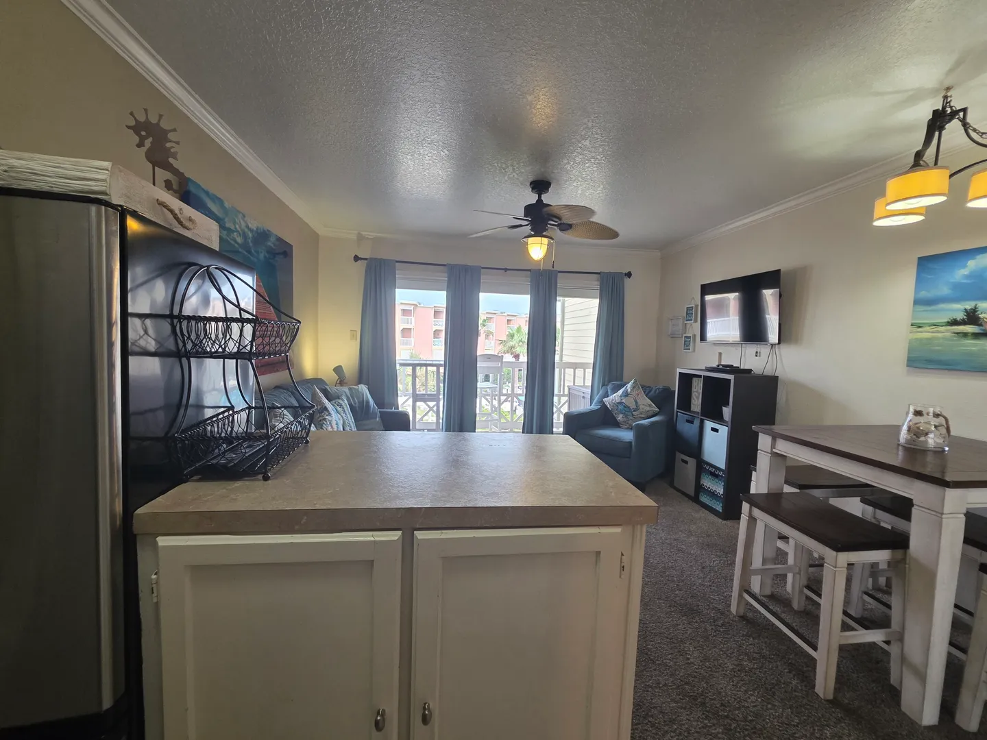 Open living area with a kitchen island in the foreground, dining table to the right, and seating near sliding glass doors.