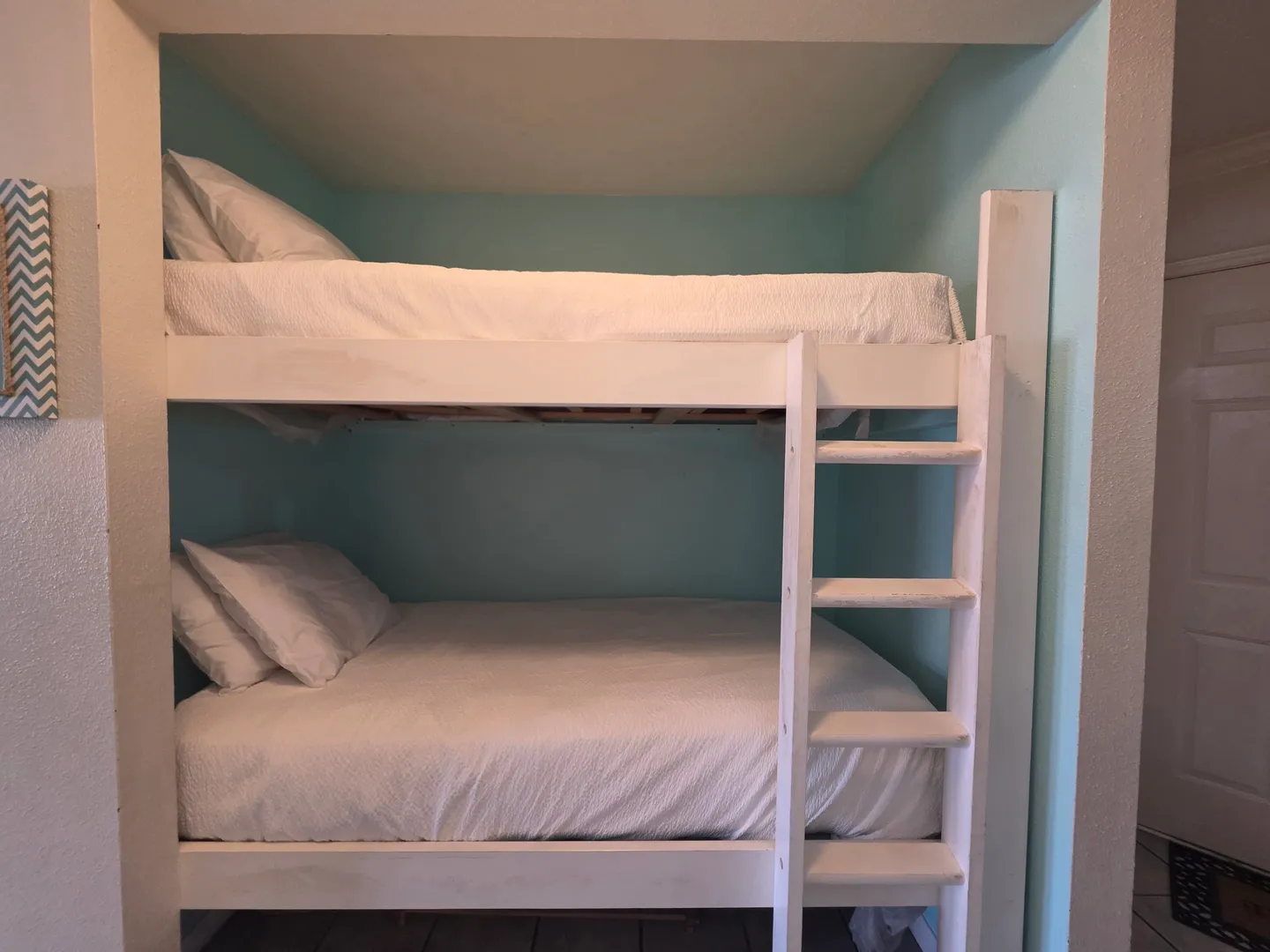 Built-in wooden bunk beds with white bedding fitted into a light blue alcove.
