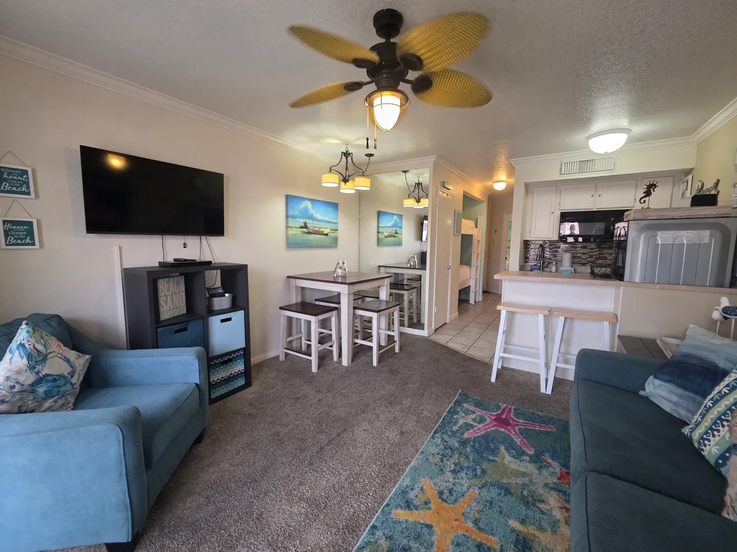 Open-concept living and dining area with carpeted floors, a wall-mounted TV, small dining table, and a kitchen pass-through counter.