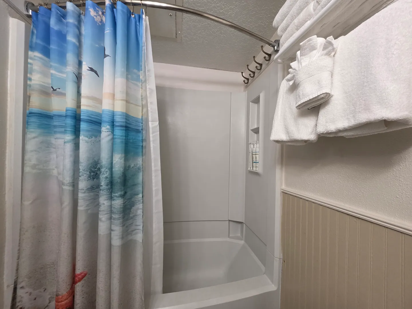 Bathroom with a bathtub and shower combination featuring an ocean-themed shower curtain and a rack with folded white towels.