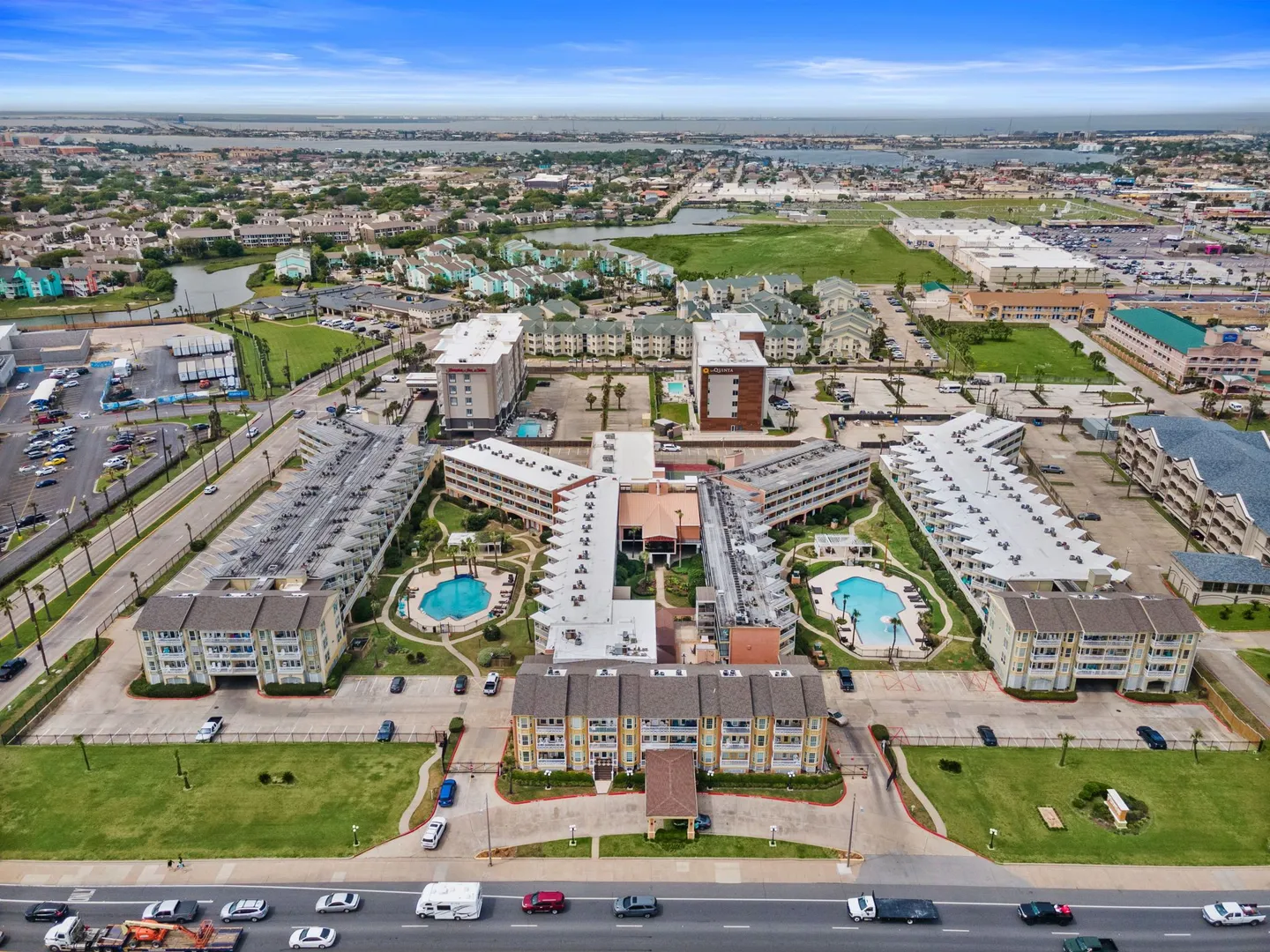 Aerial view of a sprawling multi-building resort condominium complex featuring two outdoor swimming pools and surrounding coastal landscape under a blue sky.