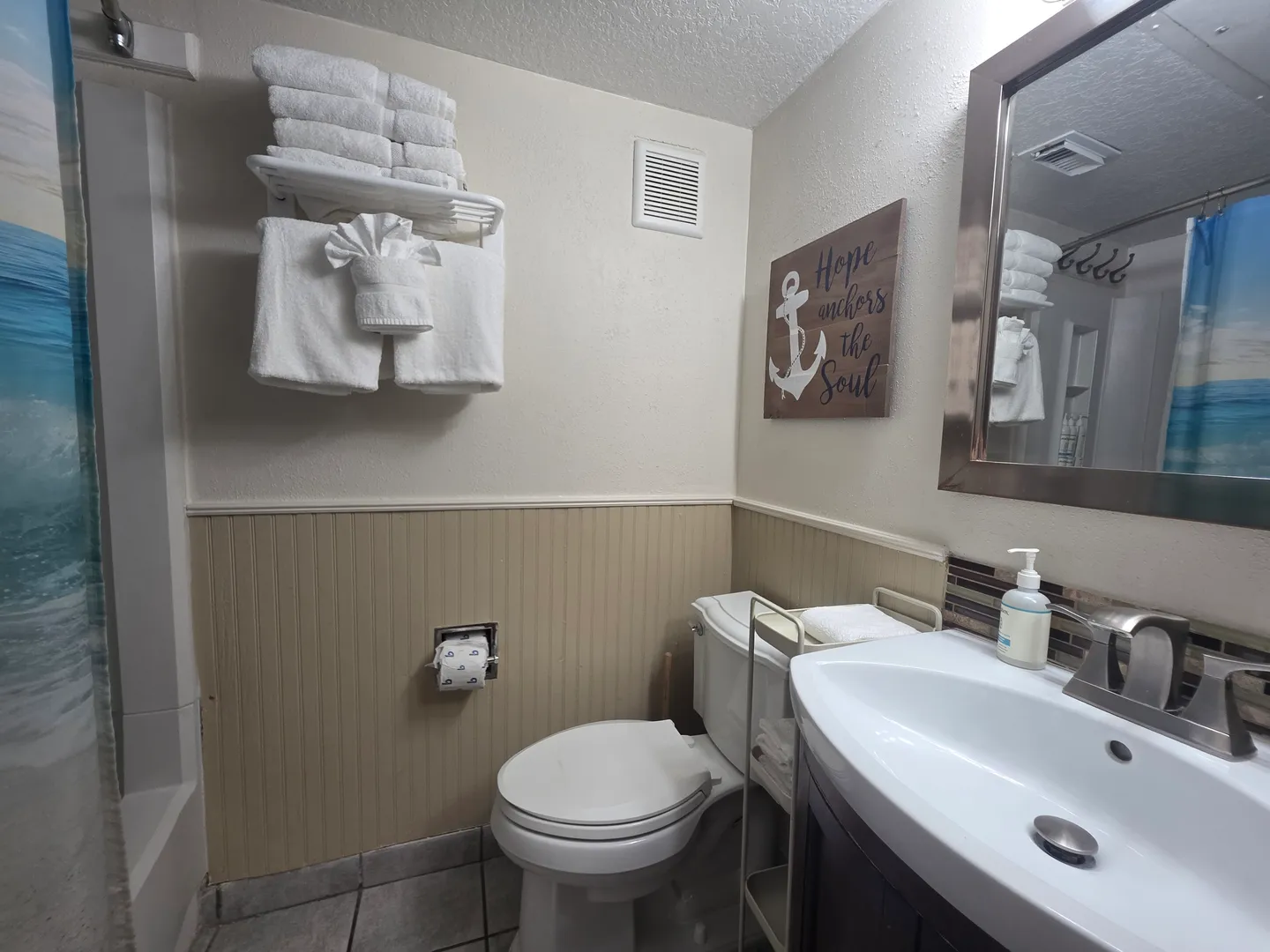 Bathroom showing a toilet, sink vanity with mirror, and stacked white towels on a wall rack.