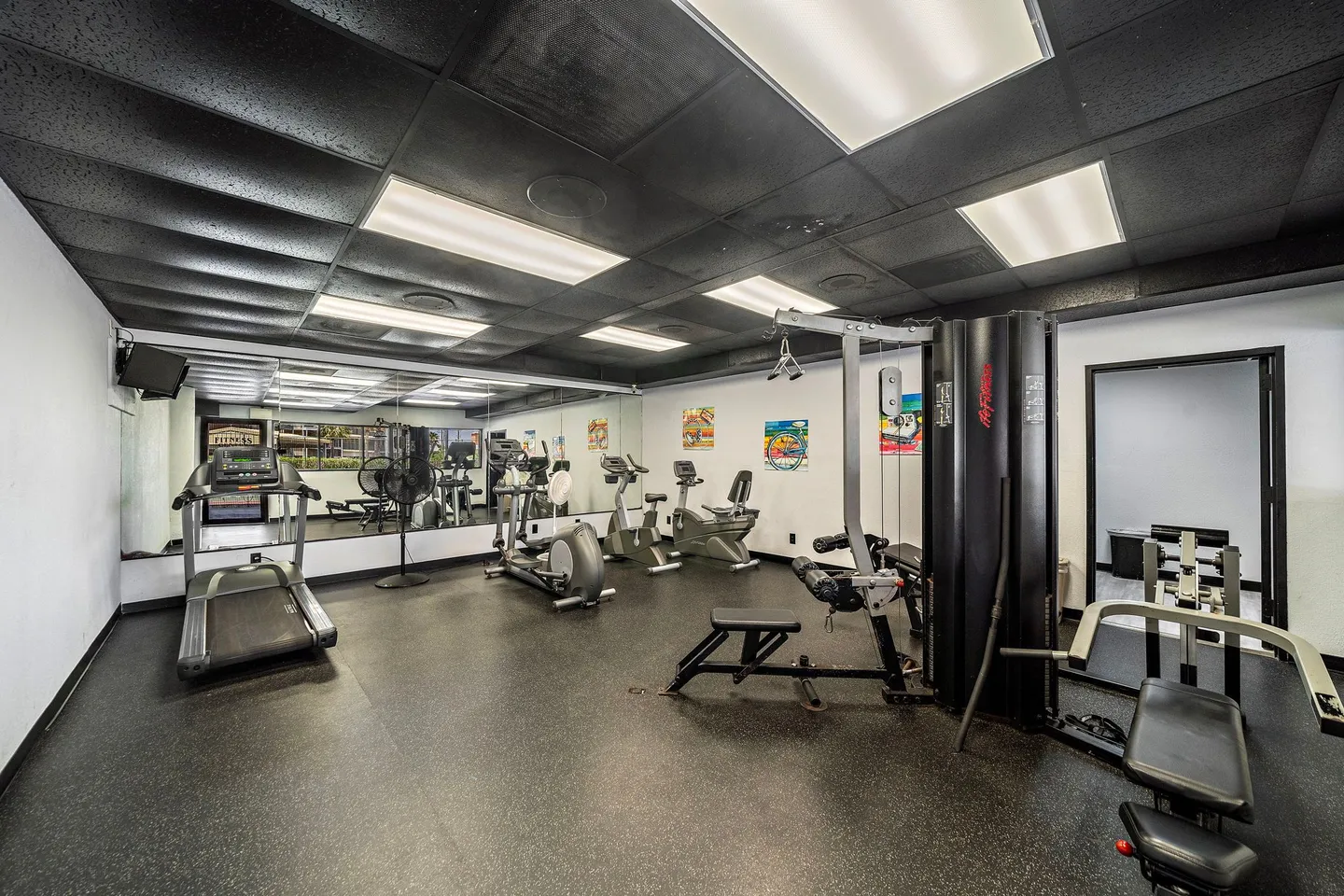Indoor fitness center with exercise equipment including treadmills, stationary bikes, and weight machines in front of a mirrored wall.