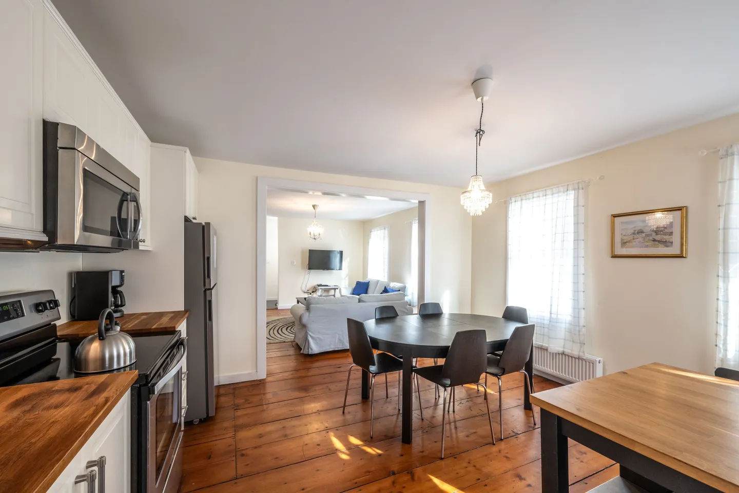Open plan dining area and kitchen with wood floors leading to an adjoining living room.