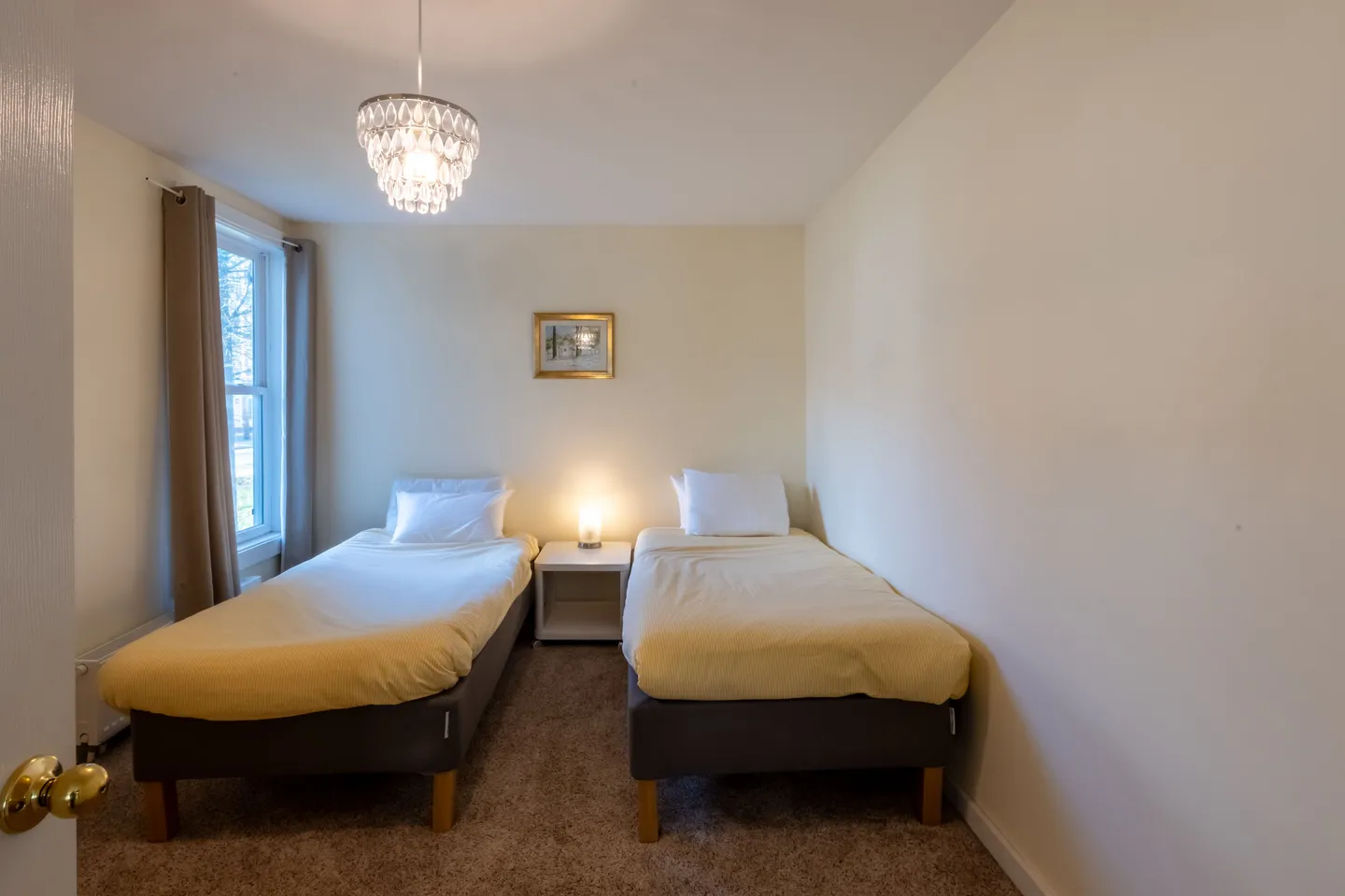 Bedroom with two single beds, a nightstand between them, carpeted flooring, and a decorative light fixture hanging from the ceiling.