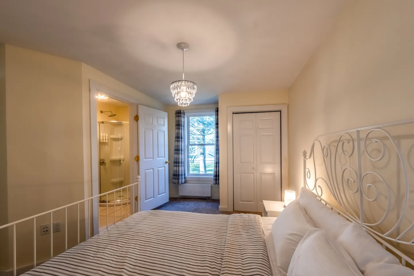 Bedroom with a white metal bed frame, patterned bedding, an en suite bathroom, closet doors, and an exterior window.