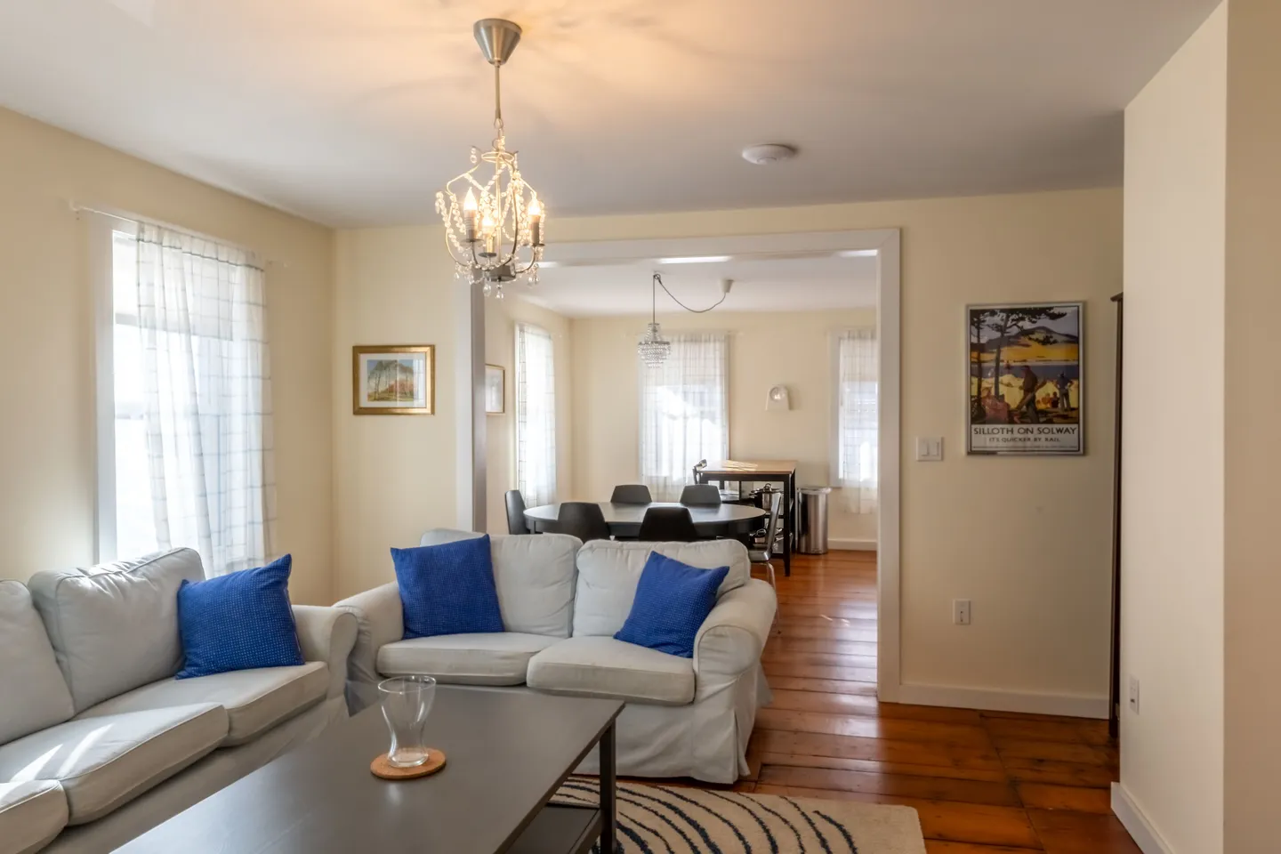 Living room with slipcovered couches and an open doorway leading into an adjoining dining area with wooden floors.
