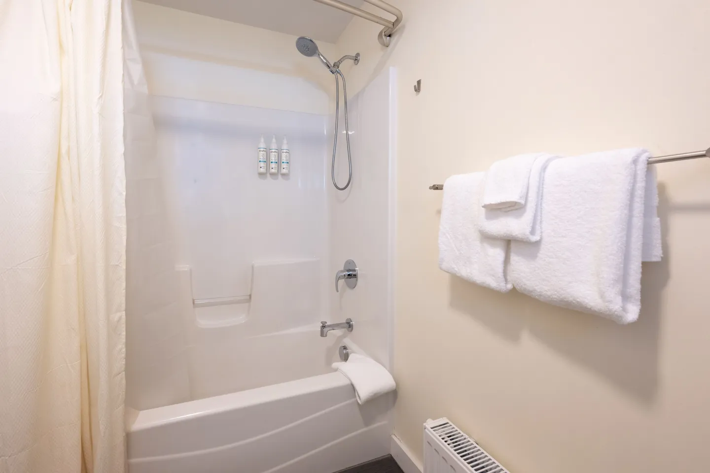Bathroom showing a white bathtub and shower combination with a shower curtain and folded white towels on a towel bar.