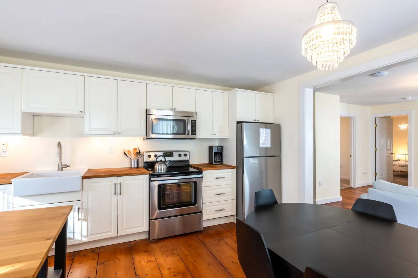 Kitchen with white cabinetry, stainless steel appliances, butcher block countertops, wide plank wood flooring, and an adjoining dining space.