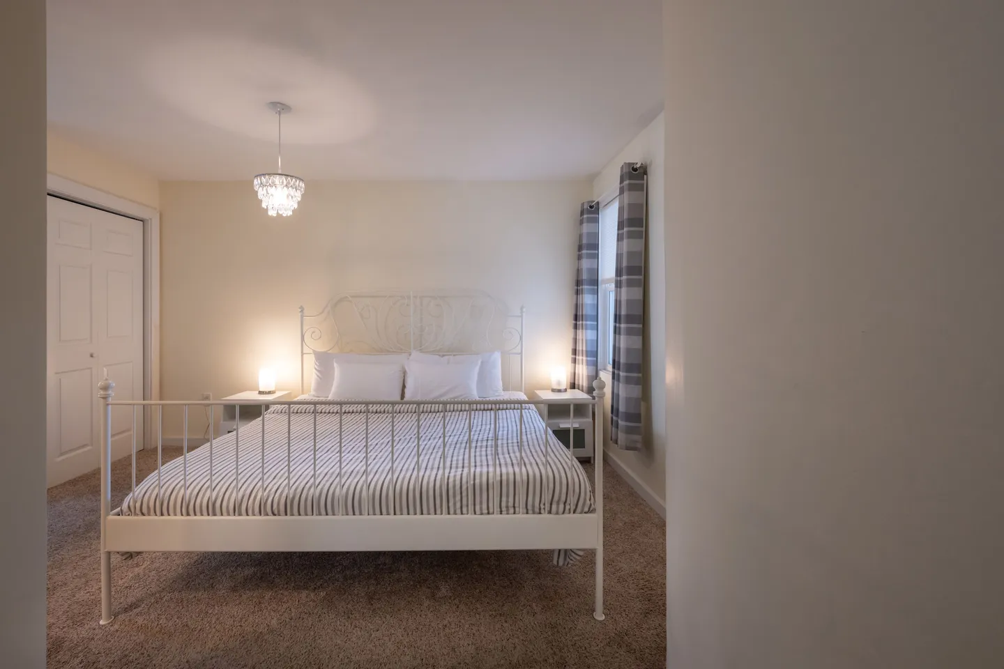 Bedroom with a white metal spindle bed, striped bedding, carpeted floor, and a crystal chandelier.