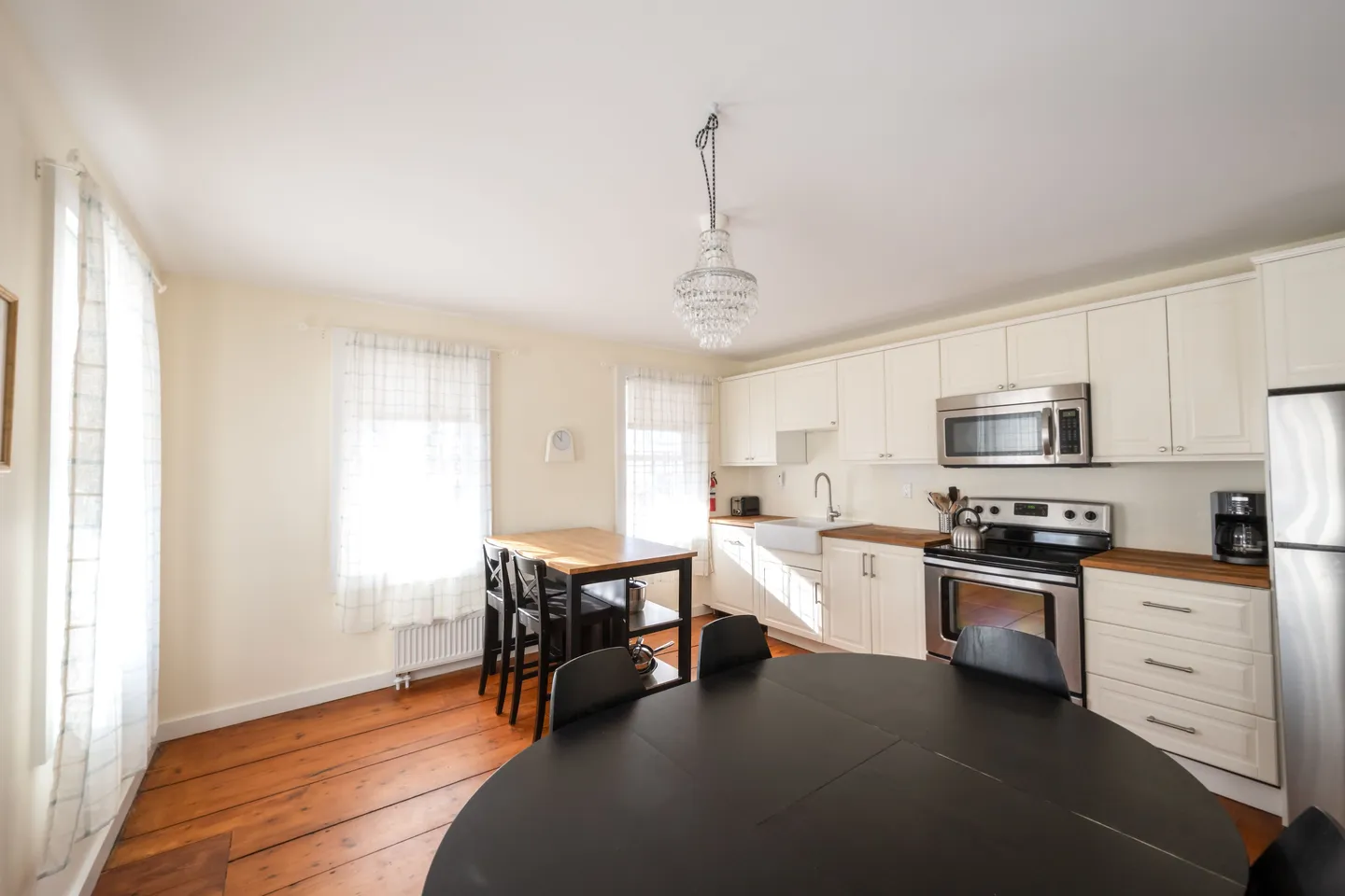 Bright kitchen and dining area with hardwood floors, white cabinetry, stainless steel appliances, and a round black dining table.