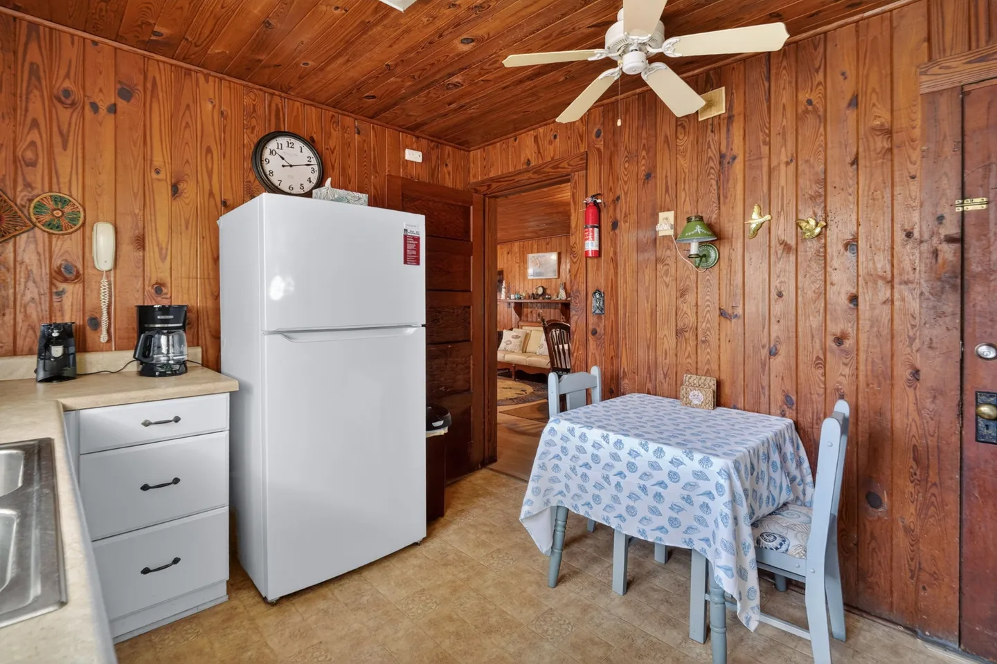 Kitchen dining nook with wood-paneled walls and ceiling, a white refrigerator, and a small table with two chairs.