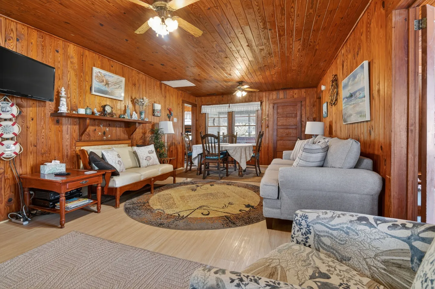 Living and dining area featuring wood-paneled walls and ceiling, a sofa, loveseat, armchairs, and a round dining table set in the background.