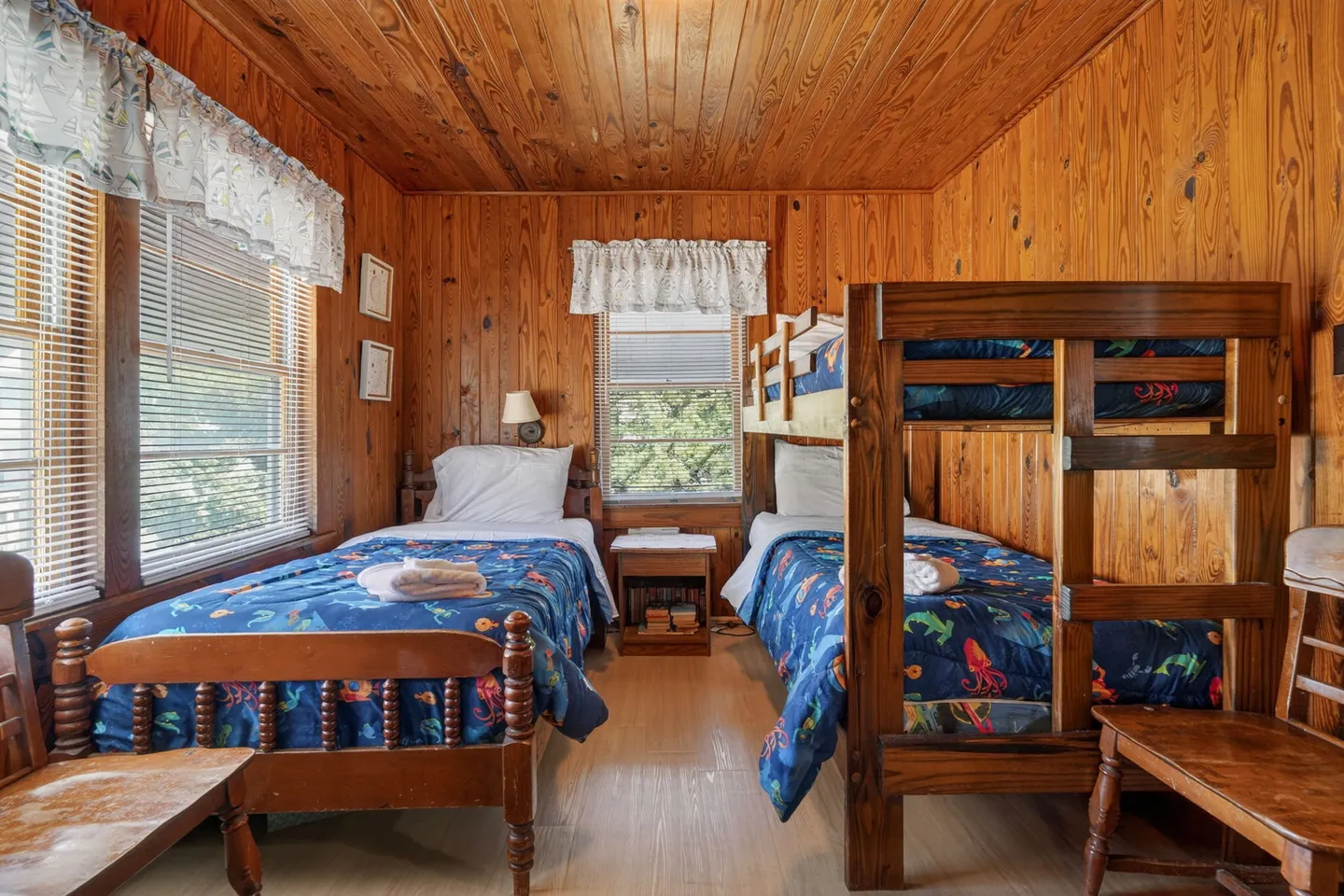 Bedroom with knotty pine paneled walls and ceiling, a single twin bed, and a wooden bunk bed with patterned blue bedding.