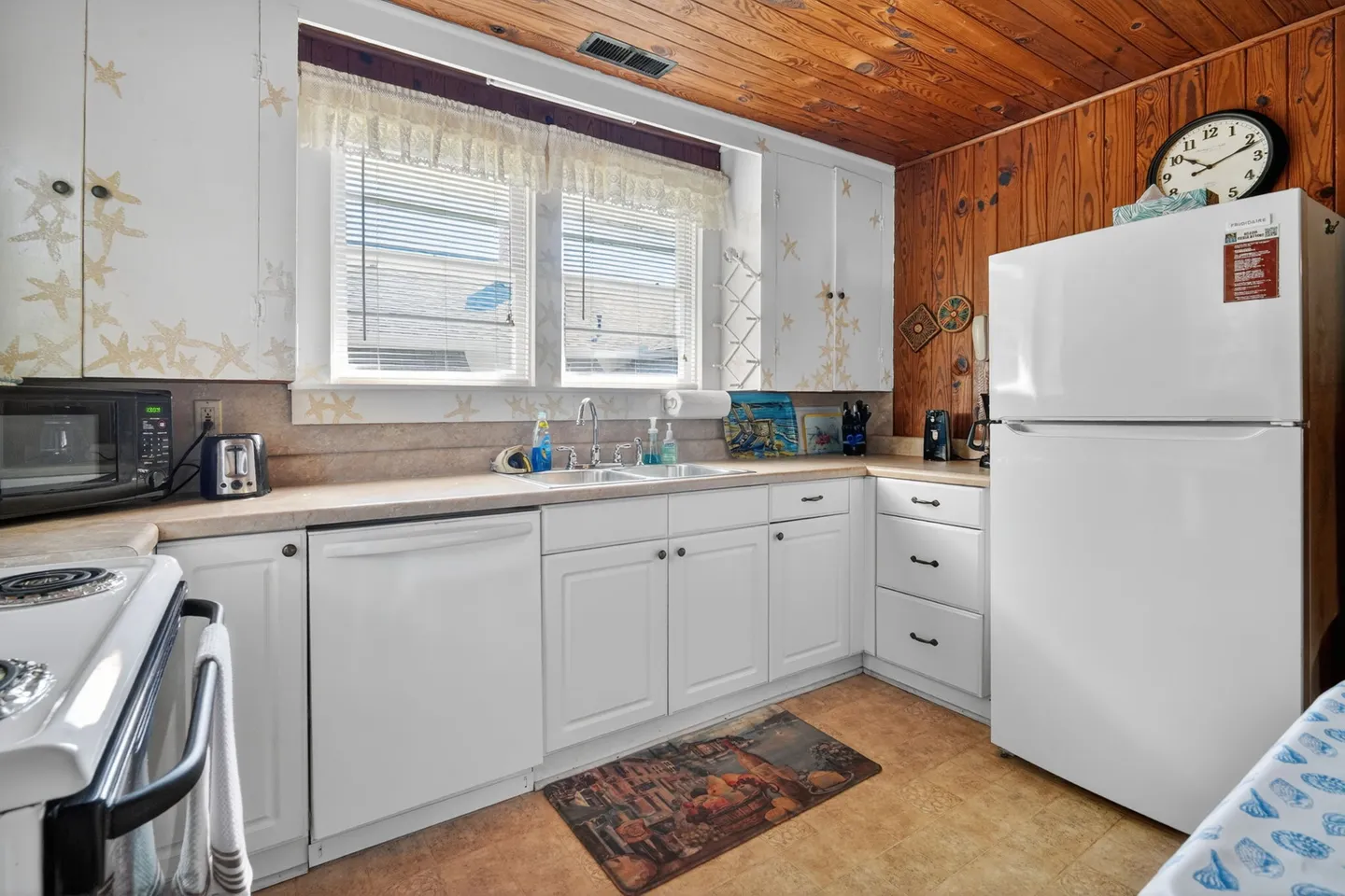 Kitchen with white cabinetry, wood-paneled ceiling and accent wall, white appliances, and a window above the sink.