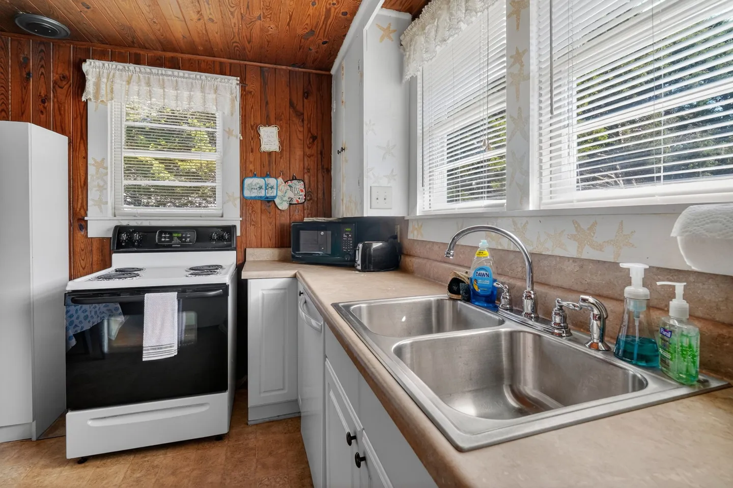 Kitchen featuring a double stainless steel sink, white electric range, and wood-paneled walls.