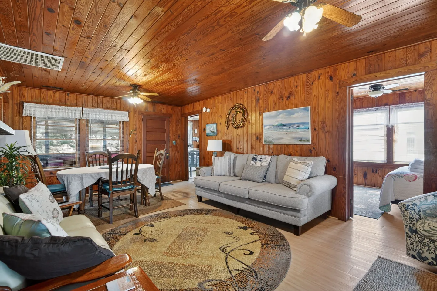 Open living and dining area with wood-paneled walls and ceiling, a gray sofa, and a dining set.