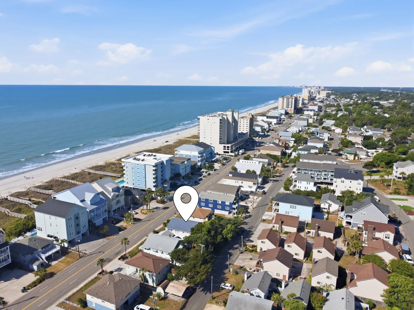 Aerial view of a coastal neighborhood with a location pin above a house near the beach and ocean.