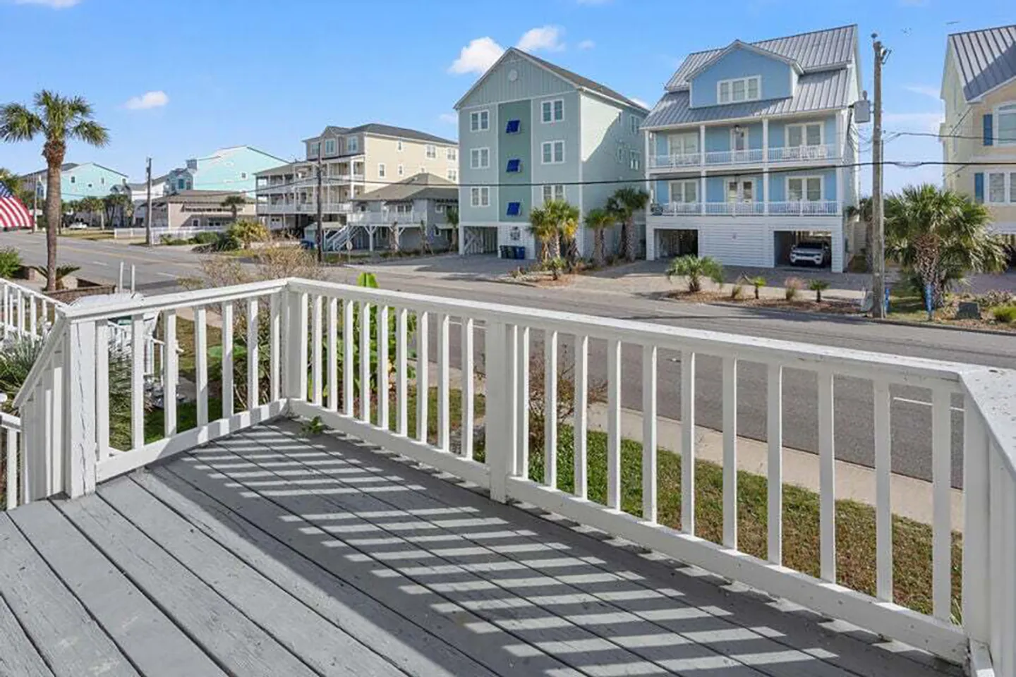 Elevated wooden deck with white railing overlooking a coastal neighborhood street with multi-story houses.