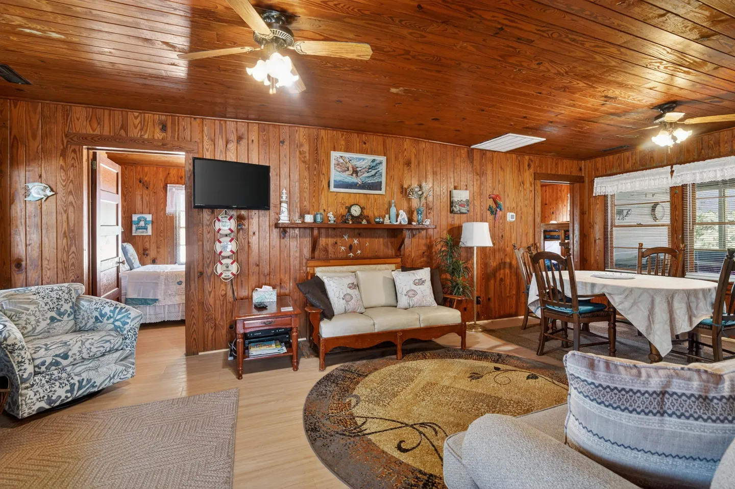 Living and dining area featuring wood-paneled walls, wood plank ceiling with ceiling fans, seating, and a dining table with chairs.