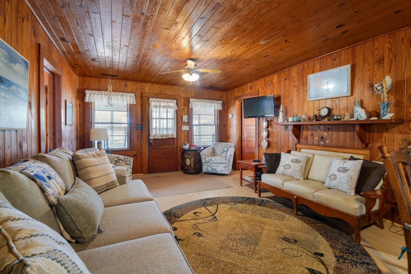 Living room with wood paneled walls, wood plank ceiling, sofas, and armchairs.