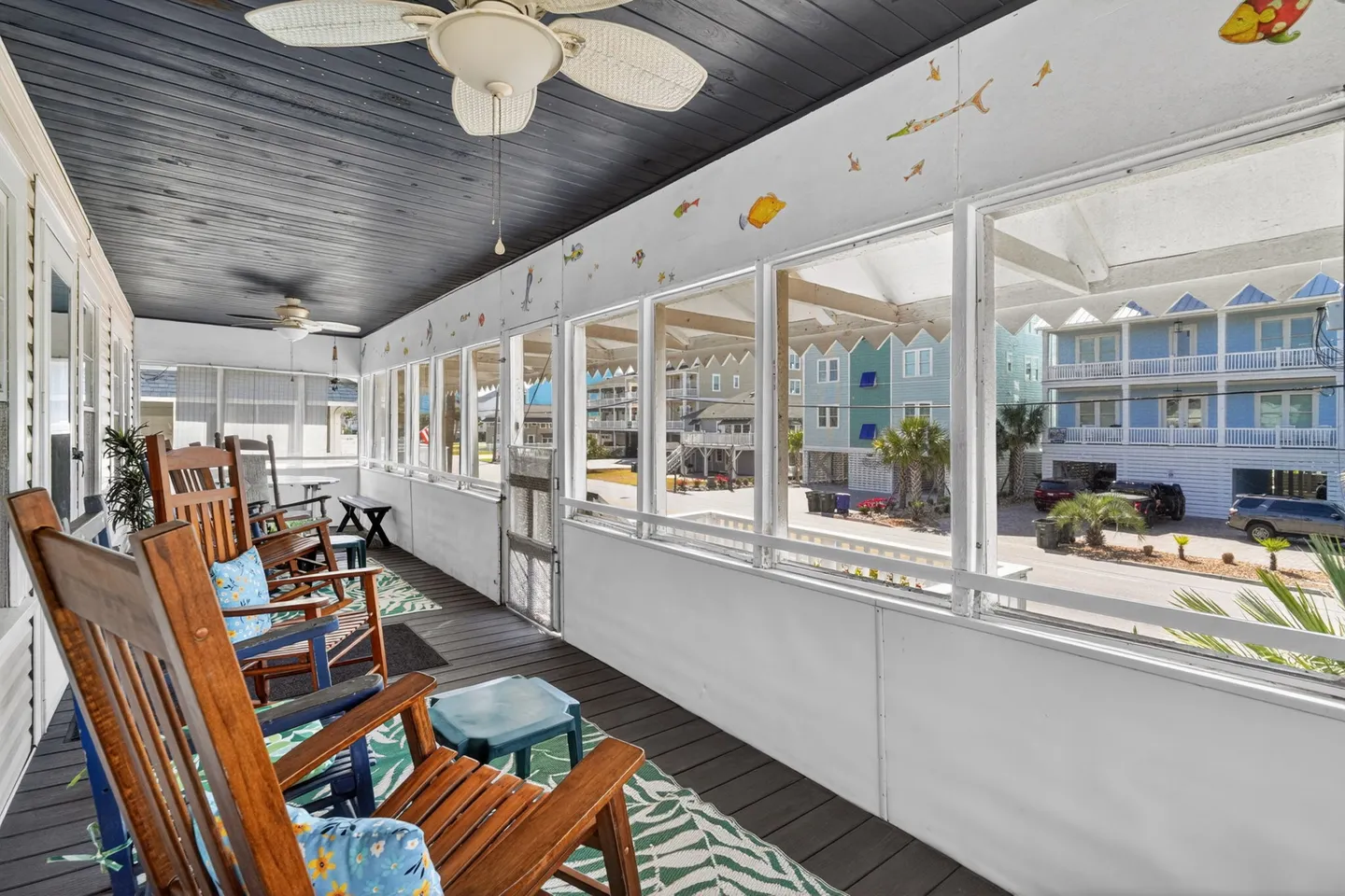 Screened porch furnished with wooden rocking chairs, ceiling fans, and views of neighboring beach homes.