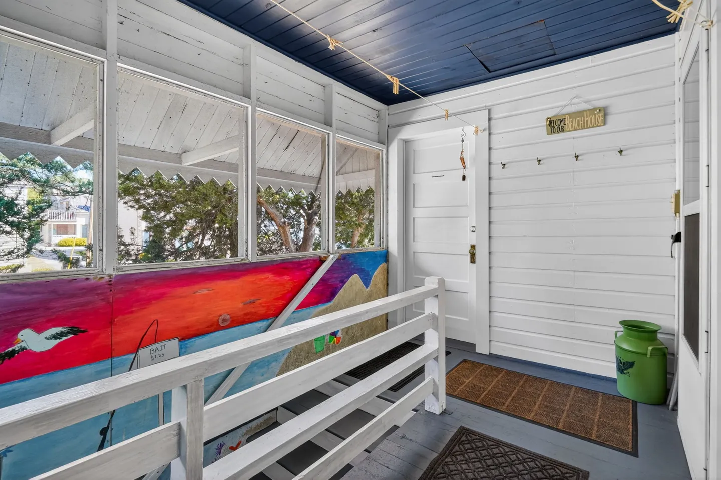 Screened porch entrance featuring white railings, a blue ceiling, and a colorful painted mural wall.