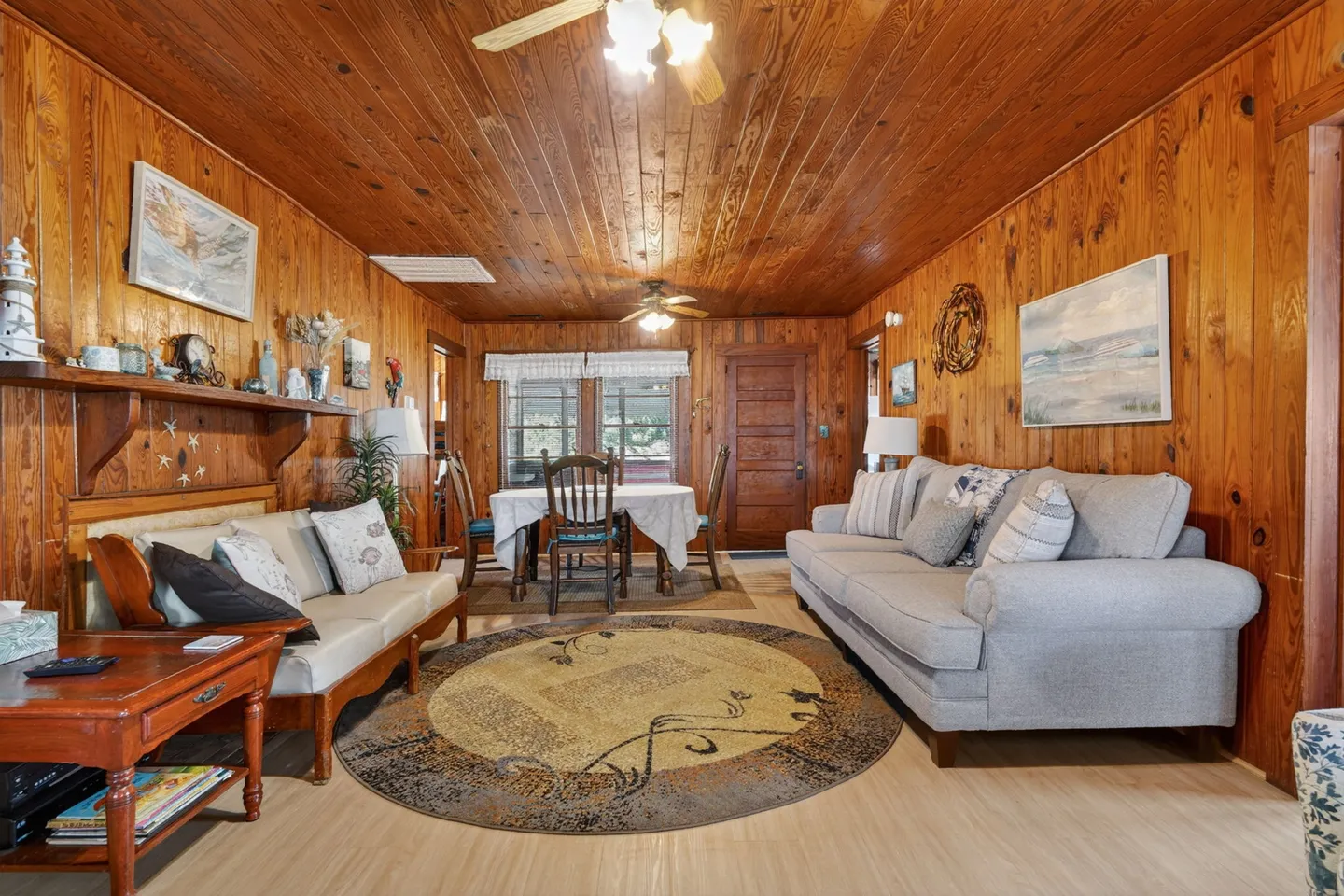 Living and dining area featuring wood-paneled walls and ceiling, a round area rug, a grey sofa, and a dining table with chairs.