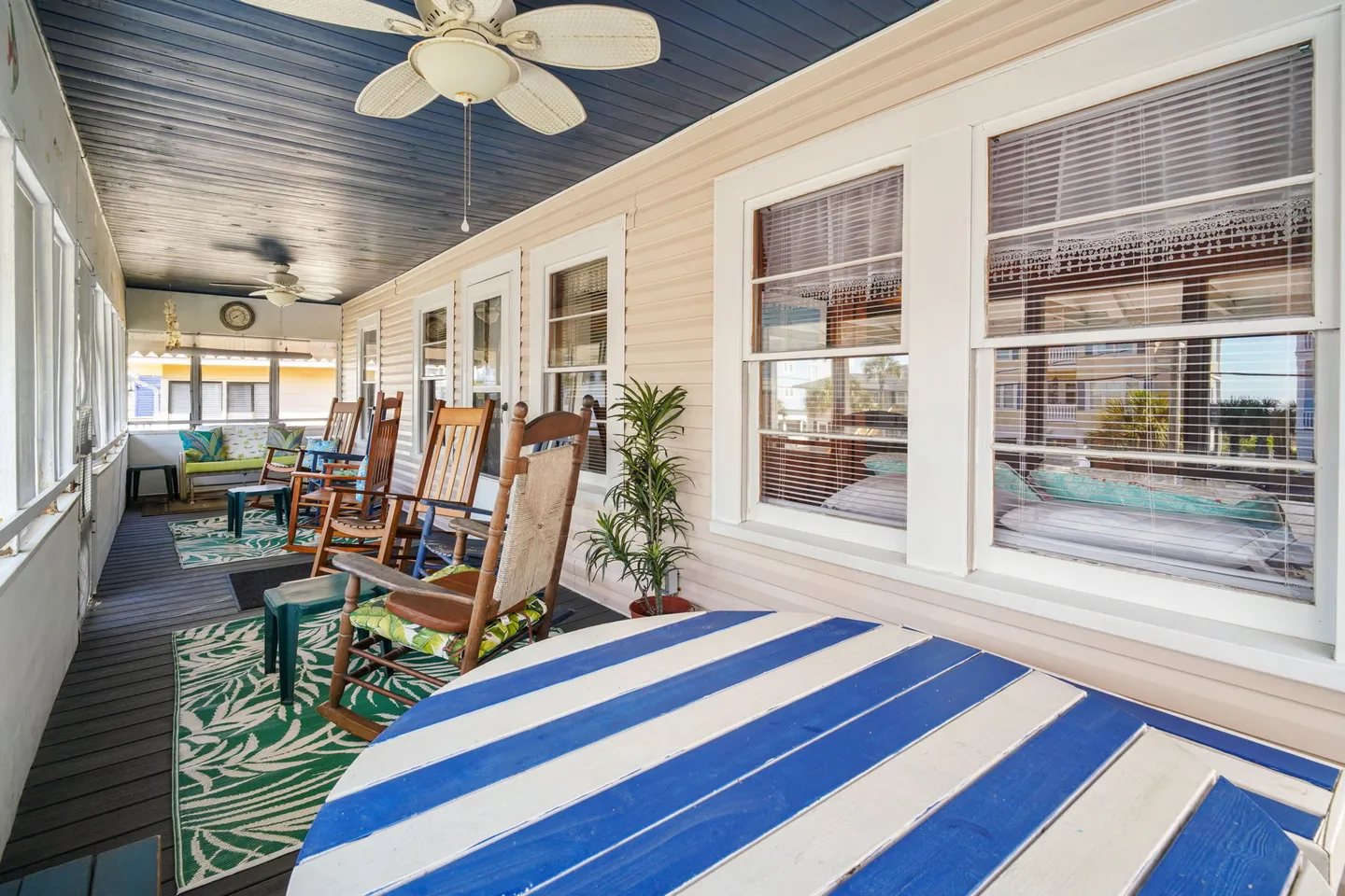 Enclosed porch with dark blue ceiling, ceiling fans, wooden rocking chairs, and striped table.